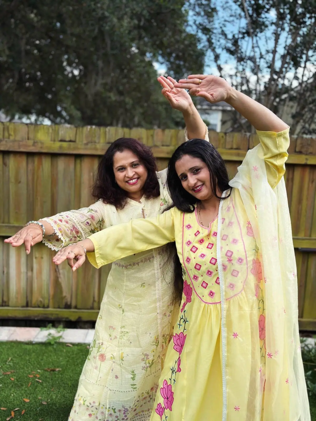 Manaswini Arts co-founders mid-pose in yellow outfits, arms extended in a dance movement outdoors.
